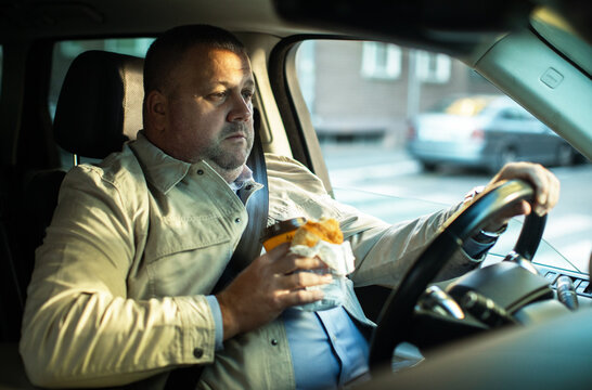 Middle-aged man eating breakfast and driving in city traffic