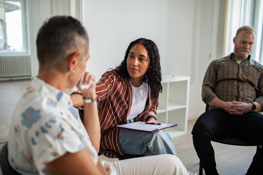 Counselor supporting adults in group therapy session indoors