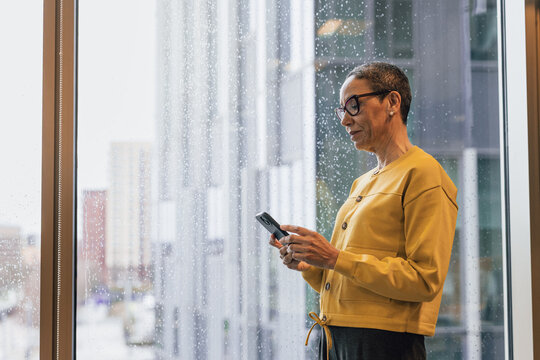 Mature Businesswoman using her phone by rainy window