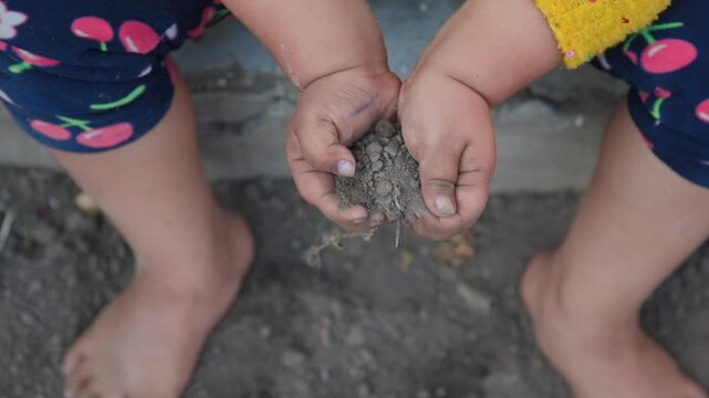 Close up of a child holding soil in hands and gently releasing it back to the ground outdoors symbolizing nature connection learning through play childhood innocence and rural lifestyle