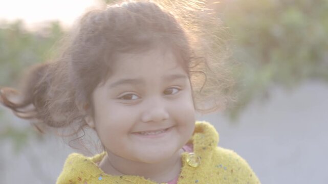Natural light video of a smiling young Indian girl looking at the camera outdoors captured in raw format symbolizing childhood innocence happiness joy and candid lifestyle moments