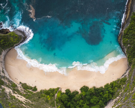 Aerial view of Kelingking Beach's dramatic cliffs plunging into the turquoise sea, with white sand meeting the foamy waves, Klungkung Regency, Bali, Indonesia.