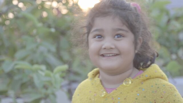 Natural light video of a smiling young Indian girl looking at the camera outdoors captured in raw format symbolizing childhood innocence happiness joy and candid lifestyle moments