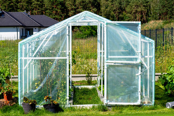 Backyard greenhouse made of foil standing on the grass behind the house.