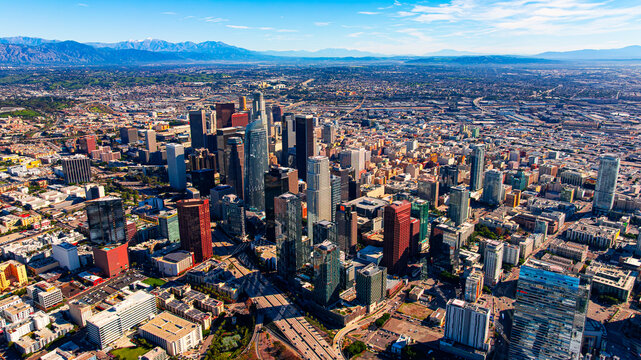 Los Angeles skyline with mountains backdrop. Daytime aerial panorama of the skyscrapers framed by distant mountain ridges and blue sky.