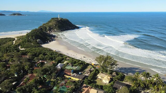 Voo sobre Ilha do Mel no litoral do Paran&aacute; em Parangu&aacute; com mar e c&eacute;u azul na praia de fora na mata atl&acirc;ntica mostrando o farol das conchas