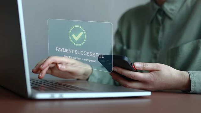 User makes a payment using a mobile phone next to a laptop with a successful transaction notice on the screen.