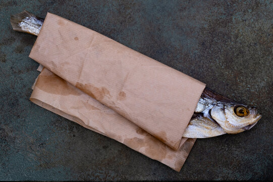 Salted dried sabrefish wrapped in brown paper on a gray surface demonstrates traditional seafood preservation packaging. Selective focus.