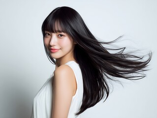 風になびく黒髪ロングヘアと白いワンピースが映える清潔感と上品さあふれる女性のスタジオポートレート