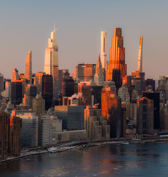 Aerial view of sunlight paints the skyscrapers in radiant gold and umber hues, reflecting off the river's icy surface, New York, New York, United States.