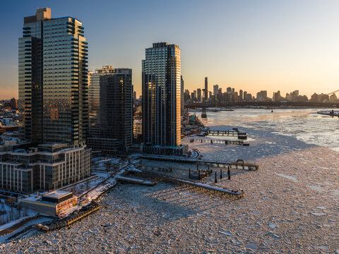 Aerial view of gleaming skyscrapers pierce the crisp winter air as the East River shimmers with ice floes, Manhattan skyline a distant silhouette, New York, New York, United States.