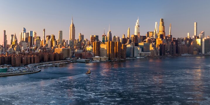 Aerial view of golden light kissing the iconic Empire State Building and other skyscrapers, with icy waters reflecting the city's majestic skyline, New York, New York, United States.