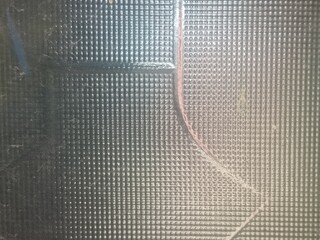 Macro Texture of Embossed Glass Surface - Detailed Pattern of Geometric Square Grid with Reflective Light on Dark Industrial Backdrop