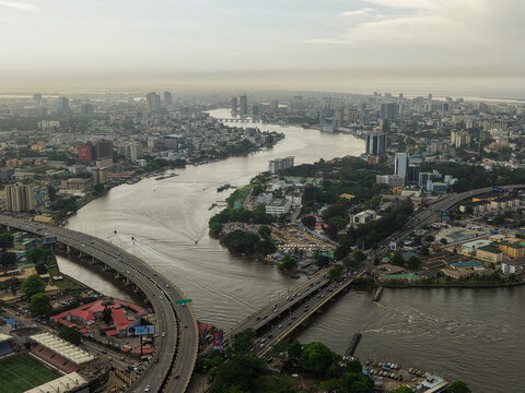 Aerial view of the muddy river winding through the urban landscape, bridges connecting the city, and skyscrapers rising against the hazy sky, Lagos, Lagos, Nigeria.