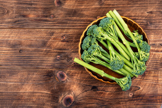Raw broccolini on a plate surrounded by natural ingredients and seasonings.