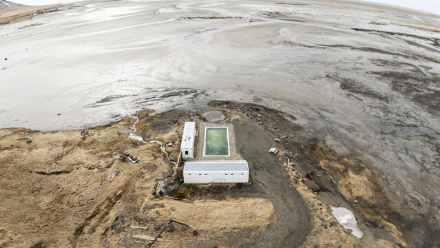 Aerial view of a rectangular pool of water surrounded by barren land and structures, a stark contrast of colors and textures, Selfoss, Iceland.