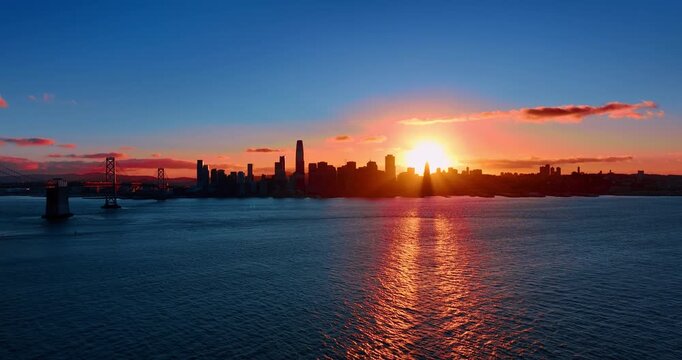 Dark silhouette of San Francisco skyline with brightly shining setting sun. Footage over the ragged waterscape of the bay at sunset.