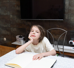 Bored schoolboy sitting with open notebook. Tired kid doing homework at table