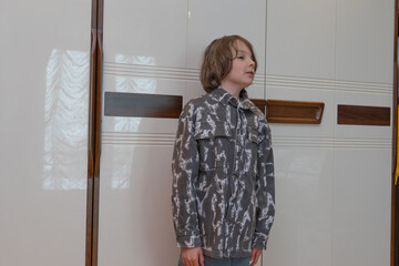 Portrait of young boy standing near wardrobe. Kid wearing casual grey shirt at home