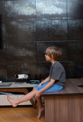 Profile of a young boy sitting on a desk at home. Bored child waiting in a modern room