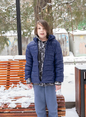 Young boy standing in snowy park. Child in blue winter jacket outdoors. Cold weather lifestyle