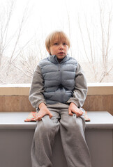 Sad young boy sitting alone near window. Unhappy child portrait indoors. Mental health concept