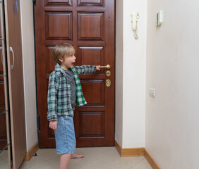 Surprised young boy reaching for door handle and shouting. Child yelling at home entrance side view