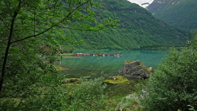 ovatnet Lake shoreline in Loen Valley, Norway. Turquoise water, mossy rocks and green mountains create a peaceful summer lakeside mood.