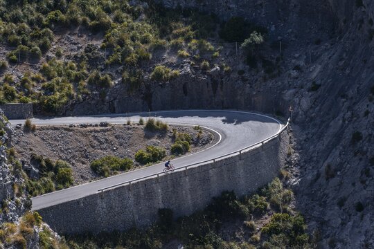 Road cyclist cycling uphill, mountain pass with serpentines to Sa Colobra, Serra de Tramuntana, Majorca, Balearic Islands, Spain