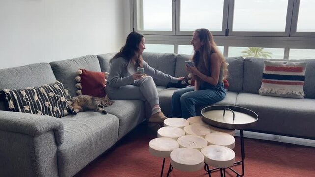 Influencer y amiga tomando caf&eacute; en el sof&aacute; acariciando a los gatos