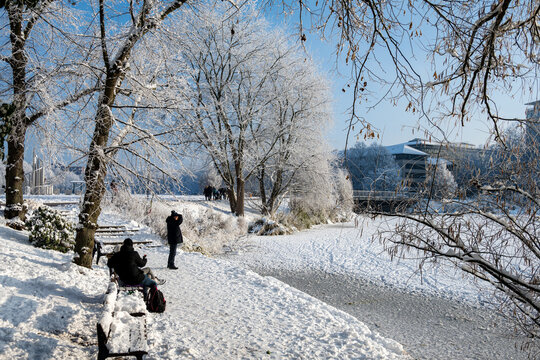 Menschen auf einer verschneiten Bank am Teich Kleiner Kiel in der Innenstadt