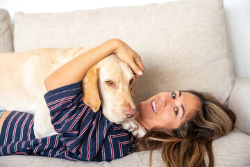 A woman is laying on a couch with a dog on her lap. The woman is smiling and she is enjoying the moment