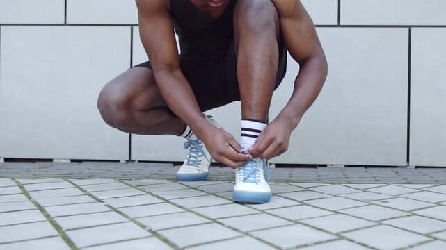 African American man in sportswear tying shoelaces on the street, athletic guy tying sneakers before training