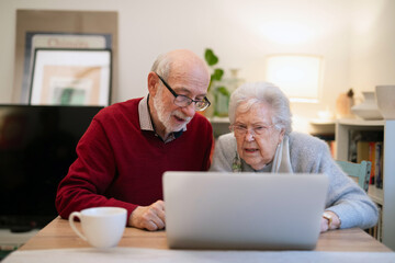 Fototapeta premium Loving elderly couple makingn online reservation, using laptop.