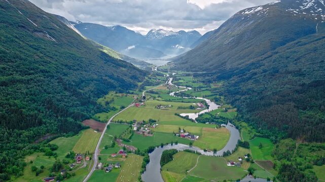 Aerial landscape of Stryn valley with winding river and patchwork farmland. Serene daytime footage framed by steep mountains and low clouds.
