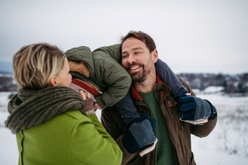 Fototapeta premium Parents and little son on walk in winter forest, during snowfall.