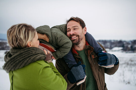 Parents and little son on walk in winter forest, during snowfall.