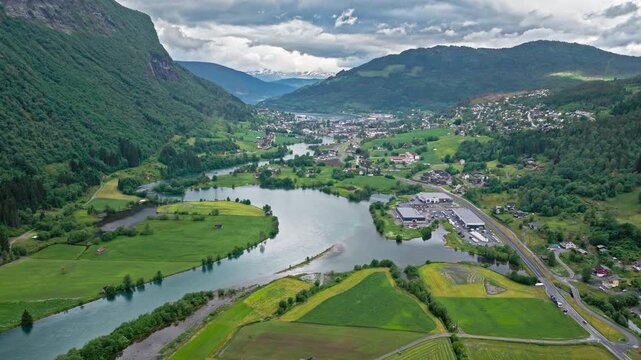 Drone footage approaching Stryn town along a river courve. Calm daytime scene blends rural landscape with small settlement and roads.