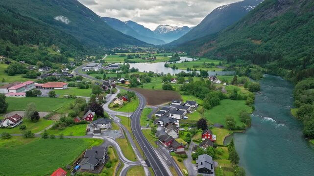 Aerial view of Stryn valley with river bends, farmland, and scattered houses in western Norway. Calm summer drone footage shows rural landscape framed by forested mountains..