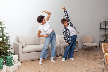 African American woman and her son do exercises at home, teenager and his mother practice yoga in...