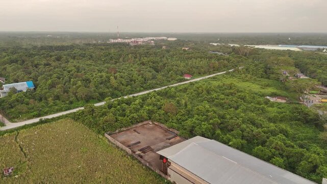 Aerial view of lush forests with winding roads and scattered industrial buildings.
