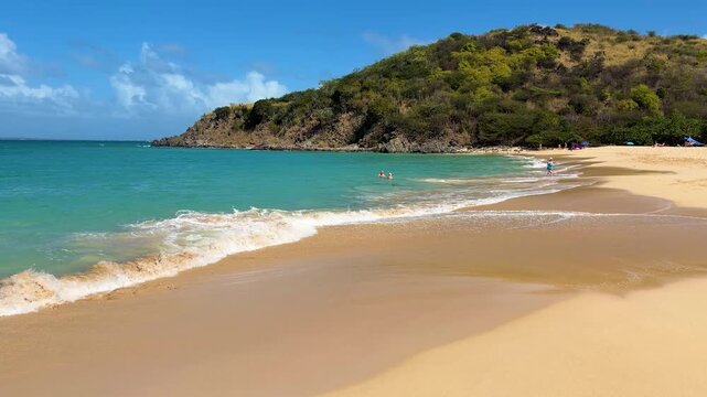 Golden sandy beach, the bright blue and turquoise waters of the Caribbean Sea and the green slopes of a low mountain on the island of St. Maarten. Saint Martin is an island in the Caribbean.