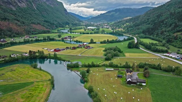 Wide drone panorama of winding river and patchwork fields in Stryn valley. Bright daylight conveys spacious rural scenery and gentle terrain.