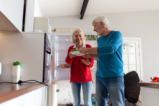 elderly couple uses refrigerator in the kitchen, gray-haired woman and her husband cook food in the kitchen and take vegetables from the refrigerator