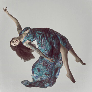 Young Woman with tattoos in a long dress floating on her back in mid air