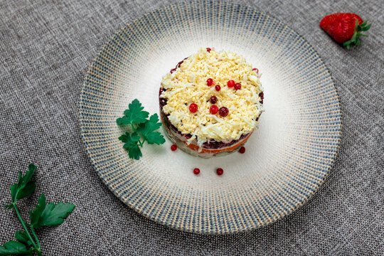 Traditional Russian layered "dressed herring" salad ("Selyodka Pod Shuboy") on a rustic plate.