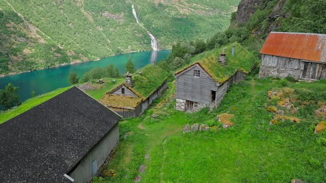 Top-down aerial view of Skagefl&aring; showing traditional Norwegian wooden houses and grass roofs. The remote farmstead overlooks the fjord far below.