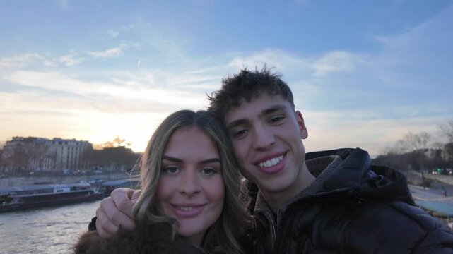 A couple in Paris is taking selfies on a bridge with the River Seine and the cityscape in the background The video is shot in a handheld POV style giving it a candid and natural feel social media cont