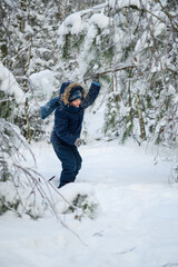 Little boy walking and playing in snowy winter forest. Natural childhood, winter season, outdoor lifestyle, family leisure, exploration and connection with nature.