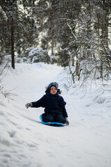 Little boy enjoying winter outdoor fun while sledding in snowy forest. Active childhood, seasonal outdoor recreation, winter adventure, family leisure and healthy lifestyle concept